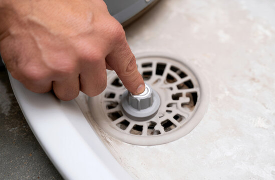 Hand Sliding Sensor Behind Water Heater Pan Edge Near Floor Drain with Clean Visual Emphasis