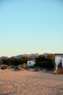 Camper trailer parked behind beach sand dunes with mountains at sunset