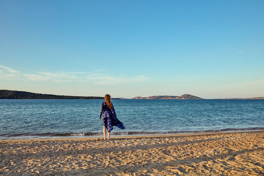 Woman standing on a sandy beach looking at the calm sea