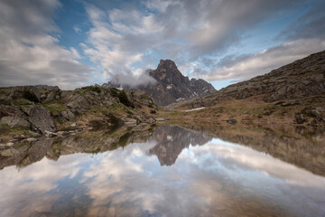 Serene alpine mountain peak mirroring on a tranquil tarn surface under scattered clouds. Ideal for wilderness travel, conservation campaigns, and outdoor adventure themes. © marcodenaro