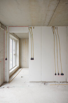Interior of an unfinished building under construction showing bare concrete walls and ceiling with electrical wiring and conduits hanging down in preparation for outlet installation