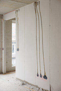 Interior of an unfinished building under construction showing bare concrete walls and ceiling with electrical wiring and conduits hanging down in preparation for outlet installation