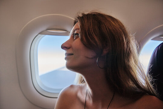 Happy Young Woman Looking Out of Airplane Window During Flight