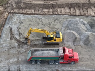 tracked excavator loads a tipper truck with gravel at a construction site  aerial view, construction development from a bird's-eye view © keBu.Medien