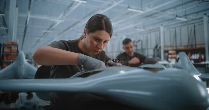 Female Aerospace Specialist Installs Multiple Electronic Boards Within Unmanned Aircraft Fuselage, Showcasing Detailed Avionics Integration and Precision Manufacturing in Modern High Tech Factory.