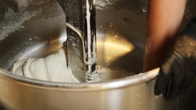 Baker hands in gloves take out dough piece of mixer drum in bakery. Employee works with automatic equipment and food products in shop