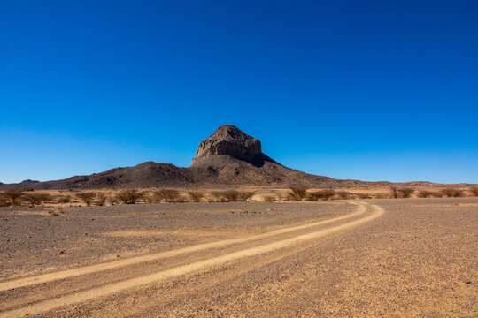 Dirt road winding toward a rocky butte in the Sahara desert, North Africa, Tamanrasset, Algeria