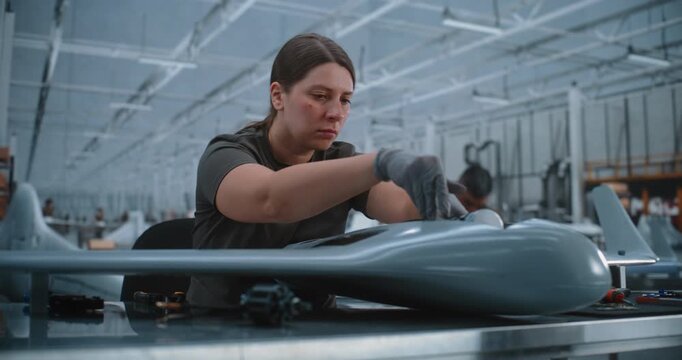 Factory Worker Mounts Custom Cylindrical Payload Sensor inside Drone Body. Massive Industrial Facility Produces Fixed Wing Unmanned Aerial Vehicles For Modern Defense Aerospace Security Sectors.