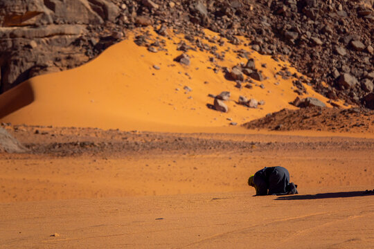 Tuareg man kneeling in prayer on a sand dune in the desert, Tassili N'Ajjer National Park, Tadrart Rouge, Algeria