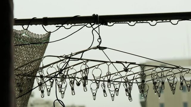 雨が降り続くベランダの物干し竿と静かに濡れるステンレスピンチハンガー