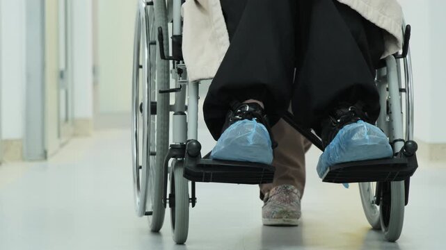 Nurse helps patient with limited mobility reach treatment room. Caregiver moves woman in wheelchair toward sterile manipulation room. Slow motion