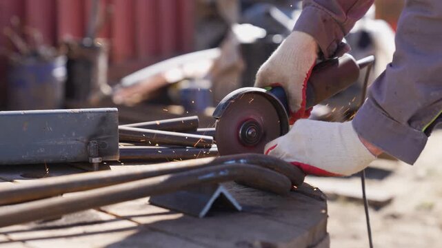 Close-up of a worker's hands cutting metal rebar with an angle grinder