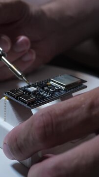 Maker soldering a microcontroller board in a 3D-printed jig, close-up