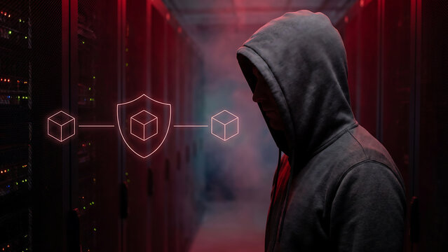 赤いサーバーラックの間で三つの立方体と盾が示すサプライチェーンを見つめるフードをかぶった人物