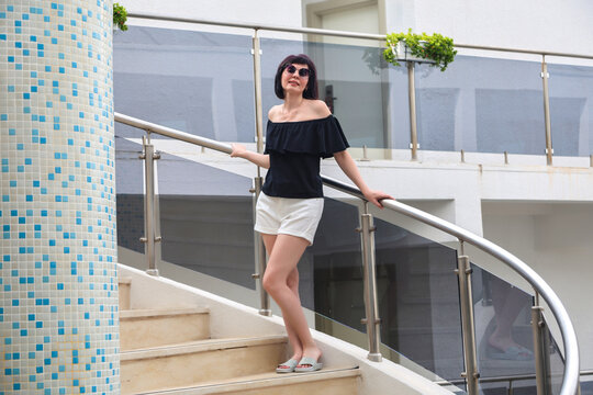Adult woman standing on external metal spiral staircase of modern building, lifestyle portrait, outdoor, daytime.
