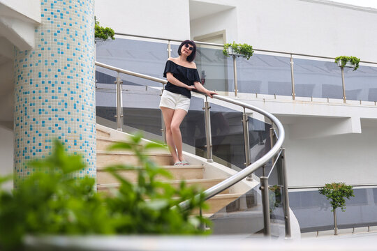woman standing on external metal spiral staircase of modern building, lifestyle portrait, outdoor, daytime.