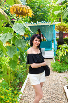 Portrait of an adult woman in shoulder clothing, on a sun-drenched alley among blooming yellow sunflowers and tall palm trees.