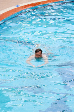Happy adult man swimming and relaxing in his own small private backyard swimming pool near a house sunny warm summer day.