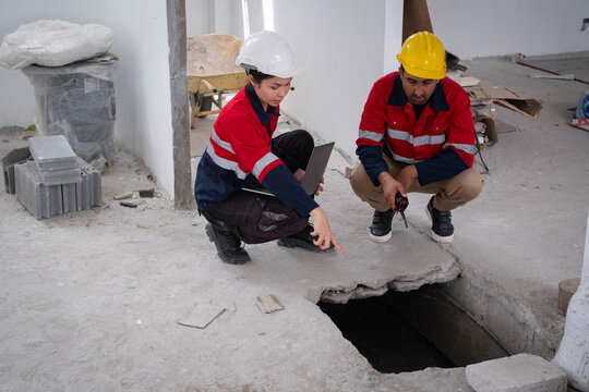 Construction engineers inspecting a damaged concrete floor opening with a laptop during structural building assessment, emphasizing foundation inspection, workplace safety, teamwork, renovation.