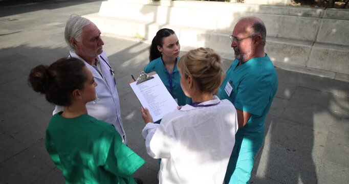 High angle view of a diverse group of doctors and nurses having a serious conversation while reviewing a patient's chart on a clipboard outside the hospital during a sunny day
