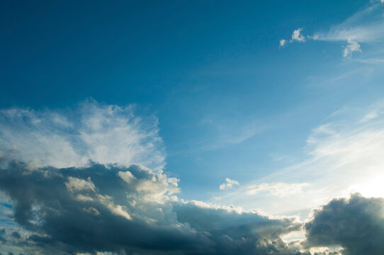 Dramatic sunset sky background. Dark grey stormy clouds and bright sunlight rays breaking through lighter clouds