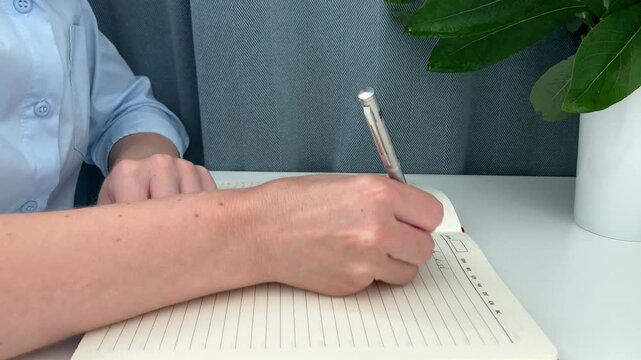 The woman writes down a to‑do list in a notebook, planning tasks for the day. The concept of effective time management, time organization, setting priorities, and increasing productivity