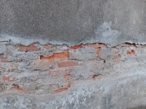 Cracked concrete wall layer revealing old red brick structure underneath close up view 
