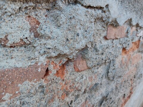 Cracked concrete wall layer revealing old red brick structure underneath close up view 