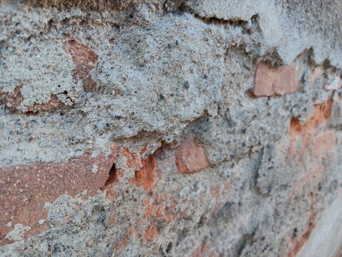 Cracked concrete wall layer revealing old red brick structure underneath close up view 