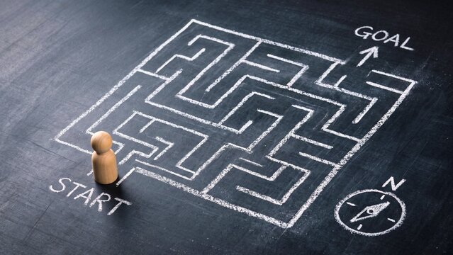 Wooden figure standing at entrance of maze toward goal on blackboard, symbolizing decision making and problem solving journey