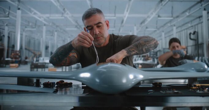 Male Engineer Installing Electronic Components and Wiring inside Unmanned Aircraft at Modern Factory, Handling Circuit Boards With Visible Chips and Capacitors, Illustrating Precision Engineering.