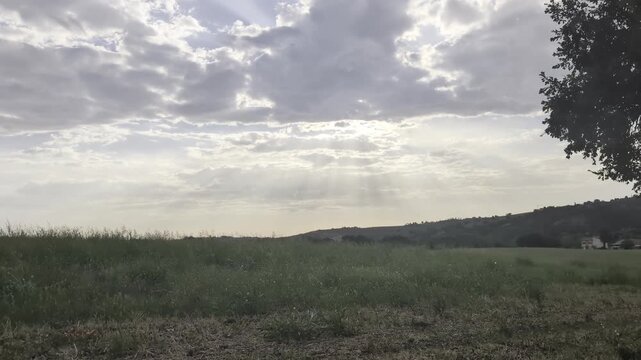 video di un paesaggio rurale in una giornata parzialmente nuvolosa, con deboli raggi di sole che filtrano nel cielo sopra un grande campo verde