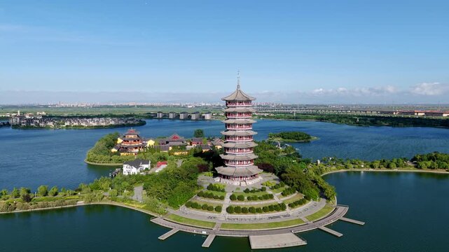 A traditional multi-tiered pagoda stands on a tree-covered island in a calm lake, under a clear blue sky.