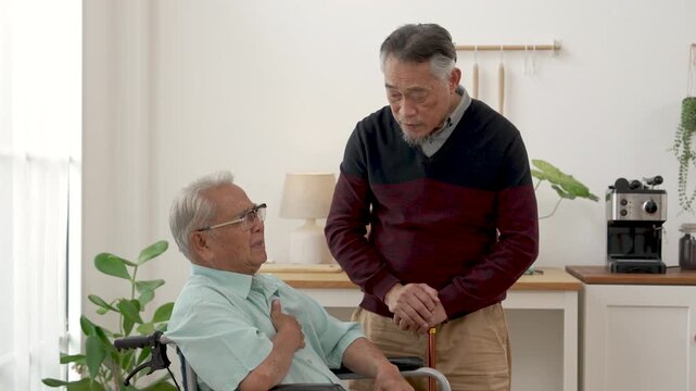 Senior Asian man touches chest while talking as concerned friend leans closer to listen in assisted living community, supporting caring friendship, reassurance, emotional comfort and wellbeing.