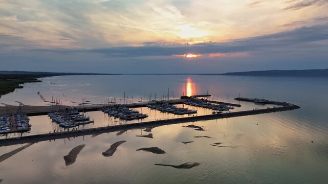 Lake Balaton at Balatonfenyves, Hungary, with marina boats, sandy shoreline and low water level at sunset, reflecting drought conditions in an aerial summer view.