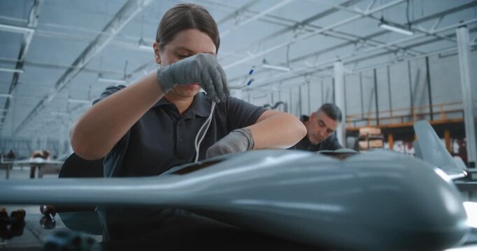 Skilled Female Engineer Carefully Integrates Electronic Boards Into Interior of Fixed Wing UAV, Highlighting Advanced Aircraft Systems Installation and Precision Assembly in Bright Modern Factory.