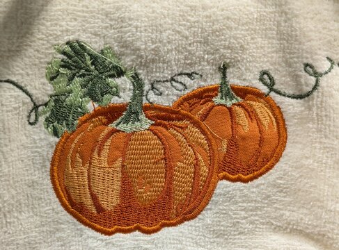 Tiempo de oto&ntilde;o. Vista de cerca de una toalla o pa&ntilde;o de cocina con bordado de calabazas con hojas y enredaderas, en colores naranja, marr&oacute;n y verde, en el expositor de una tienda	