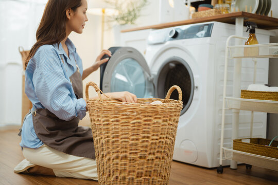 An adult kneels nearby as laundry enters a washing machine and clothes meet housekeeping beside a basket, then laundry by a washing machine leaves clothes for housekeeping in a basket during loading.