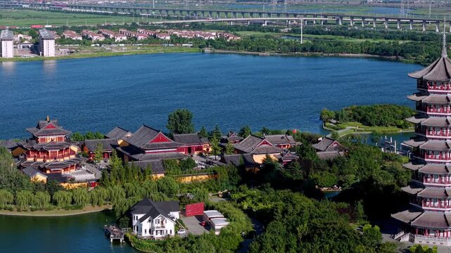 A traditional multi-tiered pagoda stands by a blue lake, with adjacent ancient-style buildings and surrounding greenery.