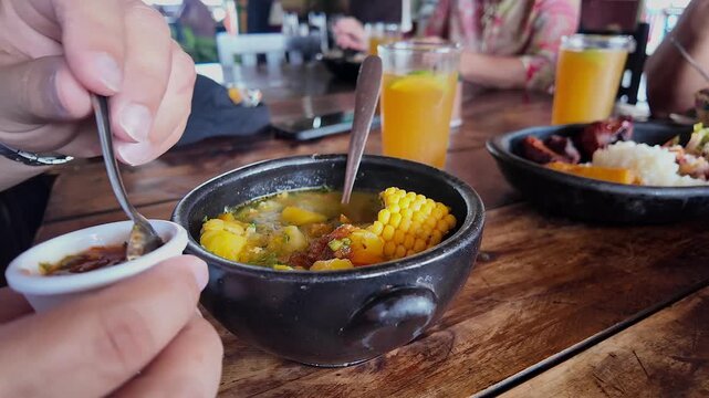 person adding sauce to traditional colombian soup bowl on wooden table