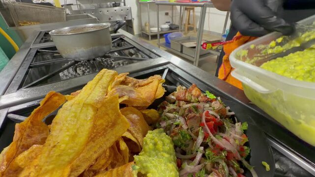 chef adding guacamole sauce to platter with plantain chips and meat salad in kitchen