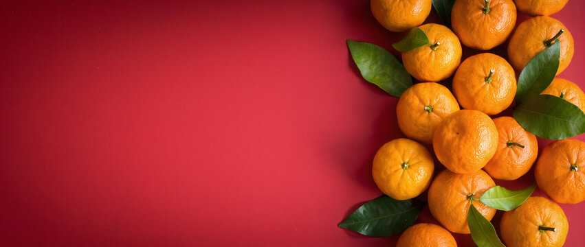Fresh mandarins with green leaves on red background. Citrus fruit top view with copy space