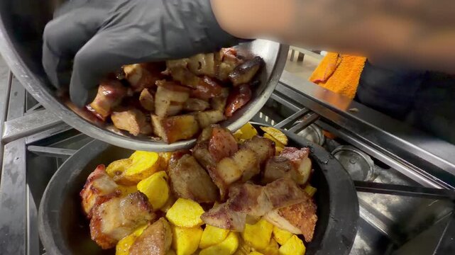 chef adding cooked pork pieces over fried potatoes in pan