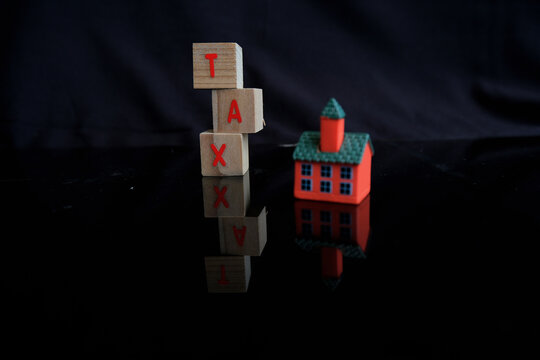 Concept of property tax based on the value of a house, building, or land, as well as local development tax: the word "tax", a house model on a dark background.