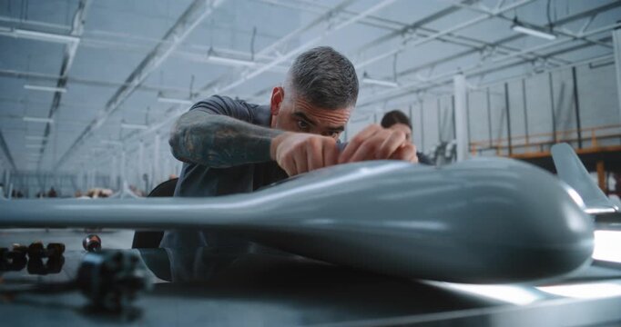 Focused Male Technician Manually Fits Hardware and Electronic Components Inside Unmanned Aircraft Body During Precision Assembly at Large Modern Aerospace Factory. Concept of Manual Assembly.
