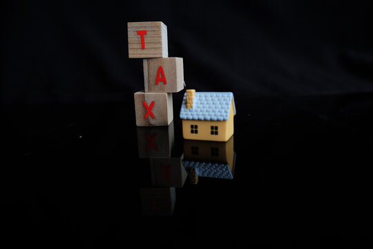 Concept of property tax based on the value of a house, building, or land, as well as local development tax: the word "tax", a house model on a dark background.