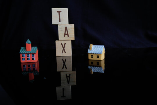 Concept of property tax based on the value of a house, building, or land, as well as local development tax: the word "tax", a house model on a dark background.