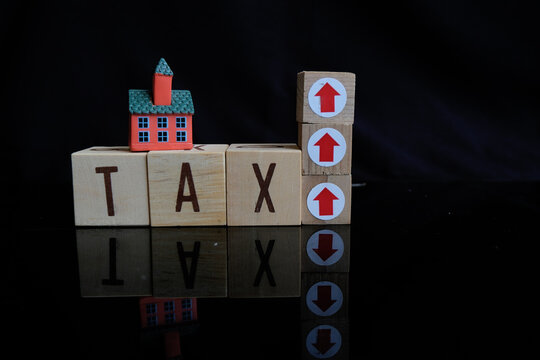 Property tax. Miniature house and tax letter on Dark background. Increase in property tax or luxury tax. Tax payment. Tax text and an upward or upward arrow symbol