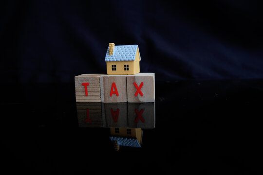 Concept of property tax based on the value of a house, building, or land, as well as local development tax: the word "tax", a house model on a dark background.