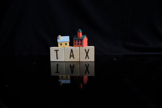Concept of property tax based on the value of a house, building, or land, as well as local development tax: the word "tax", a house model on a dark background.